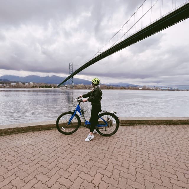 Shaye Davoodi cycling beside the water under a bridge.